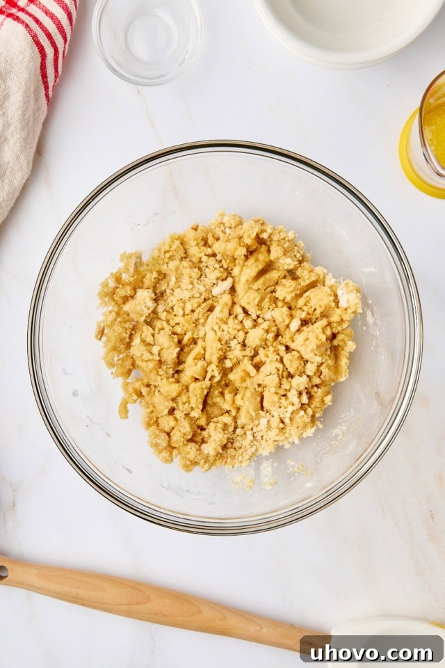 The crumb topping mixture in a glass mixing bowl, after melted butter has been stirred in, creating small, cohesive crumbs.