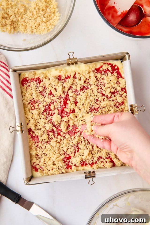 Buttery crumb topping being generously sprinkled over the strawberry layer of the cheesecake bars, just before baking.