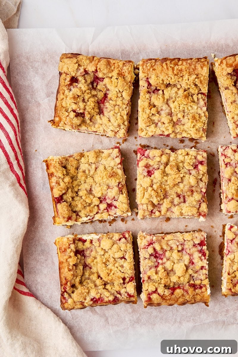 Overhead view of perfectly sliced strawberry cheesecake bars arranged neatly on parchment paper, showcasing their distinct layers of crust, cheesecake, strawberry, and crumb.