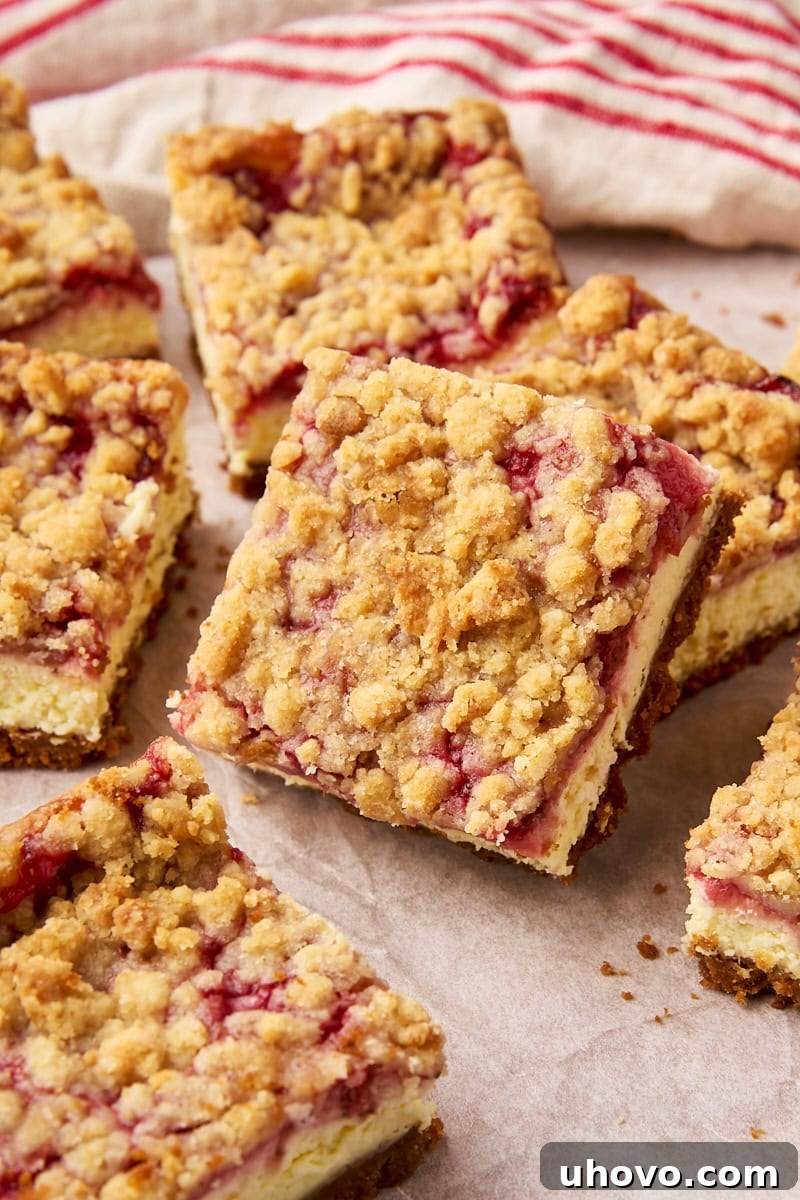 An inviting assortment of fresh strawberry cheesecake bars casually scattered on a sheet of parchment paper, highlighting their vibrant color and crumbly topping.