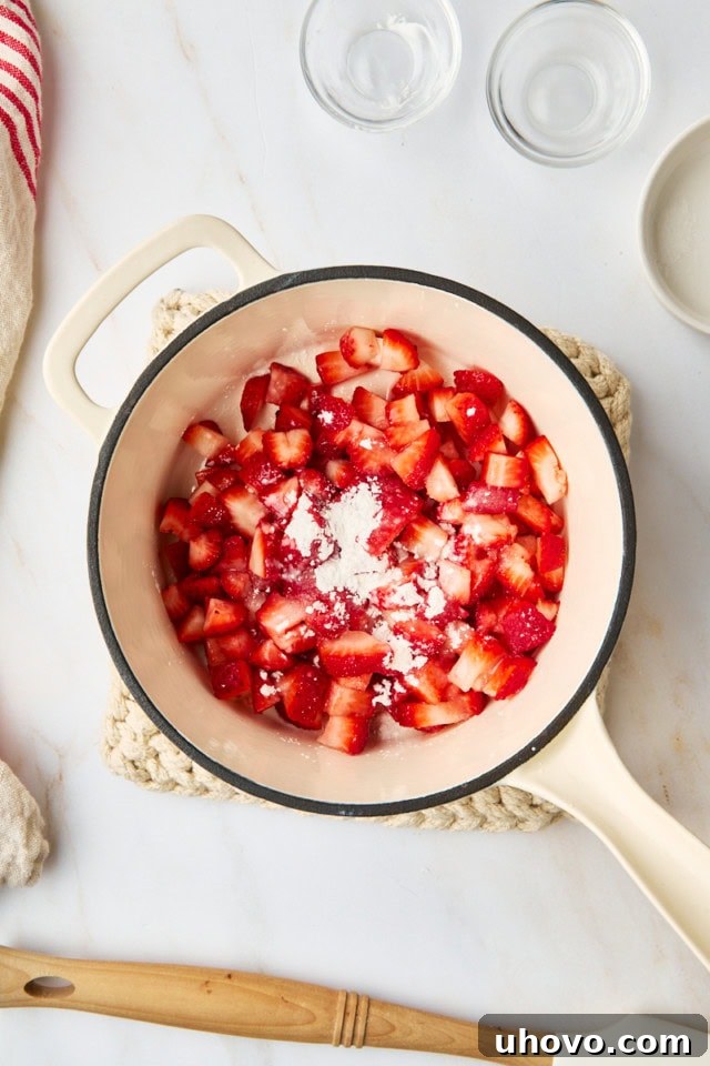 Ingredients for the strawberry topping—chopped fresh strawberries, granulated sugar, a splash of lemon juice, and a sprinkle of cornstarch—combined in a saucepan, ready for cooking.