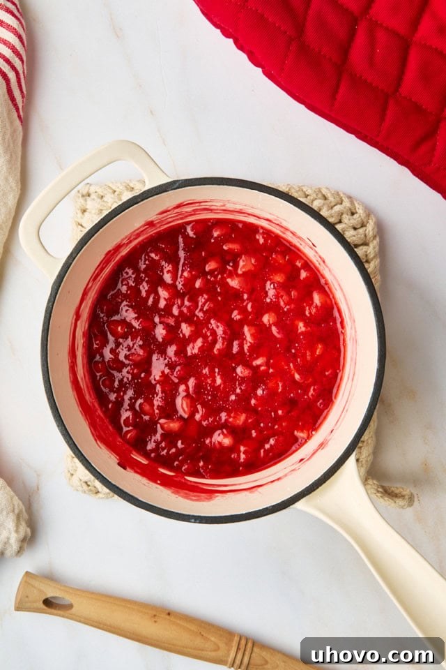 Close-up overhead view of the cooked strawberry topping simmering in a saucepan, showing its thickened, jammy consistency with soft berry pieces.