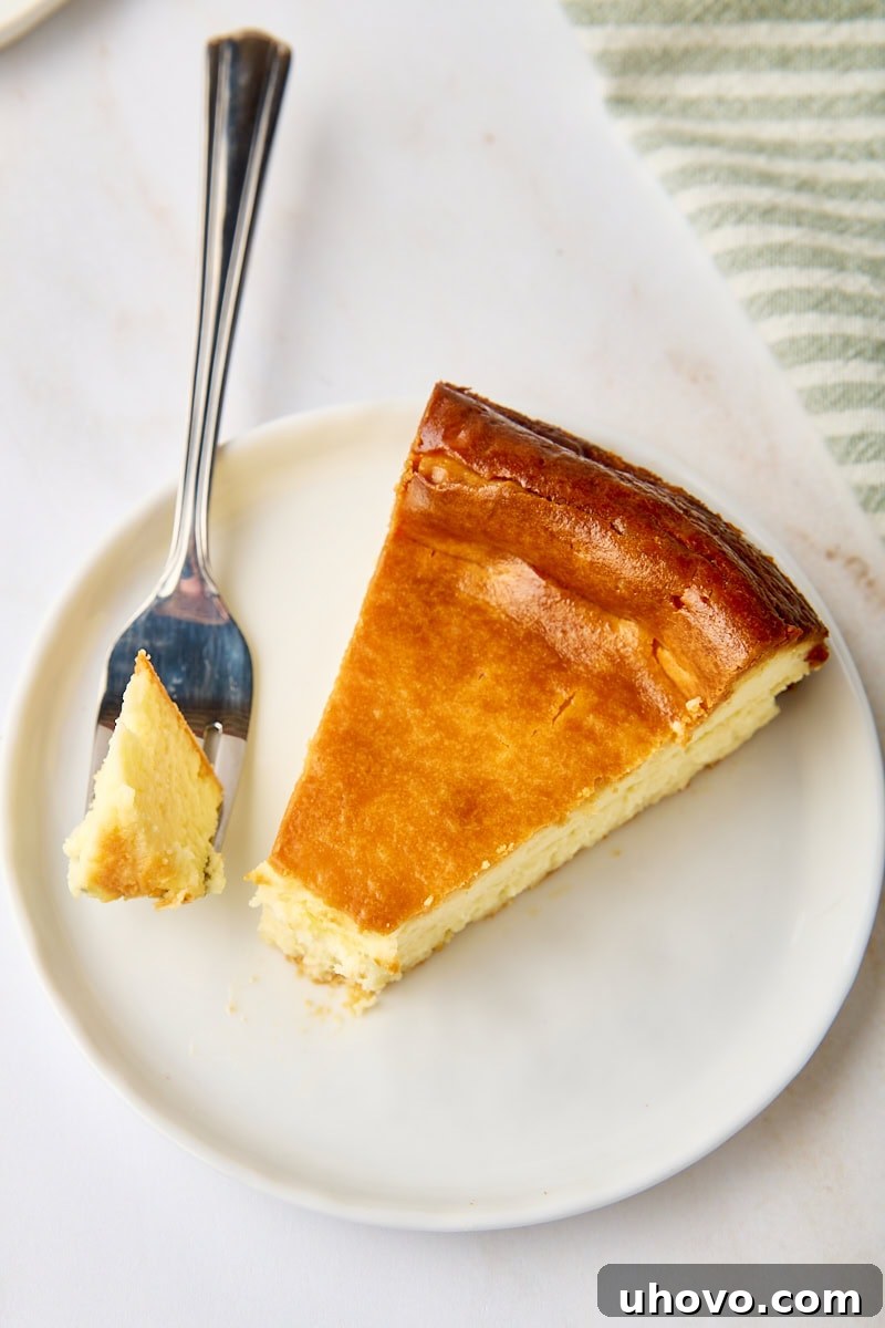 Another enticing shot of a New York cheesecake slice on a white plate, with a fork gently positioned, inviting the viewer to savor its creamy perfection.