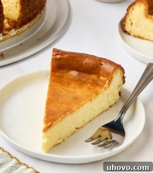 A slice of New York cheesecake on a white plate with a fork, and more cheesecake partially visible in the background, highlighting its rich texture.