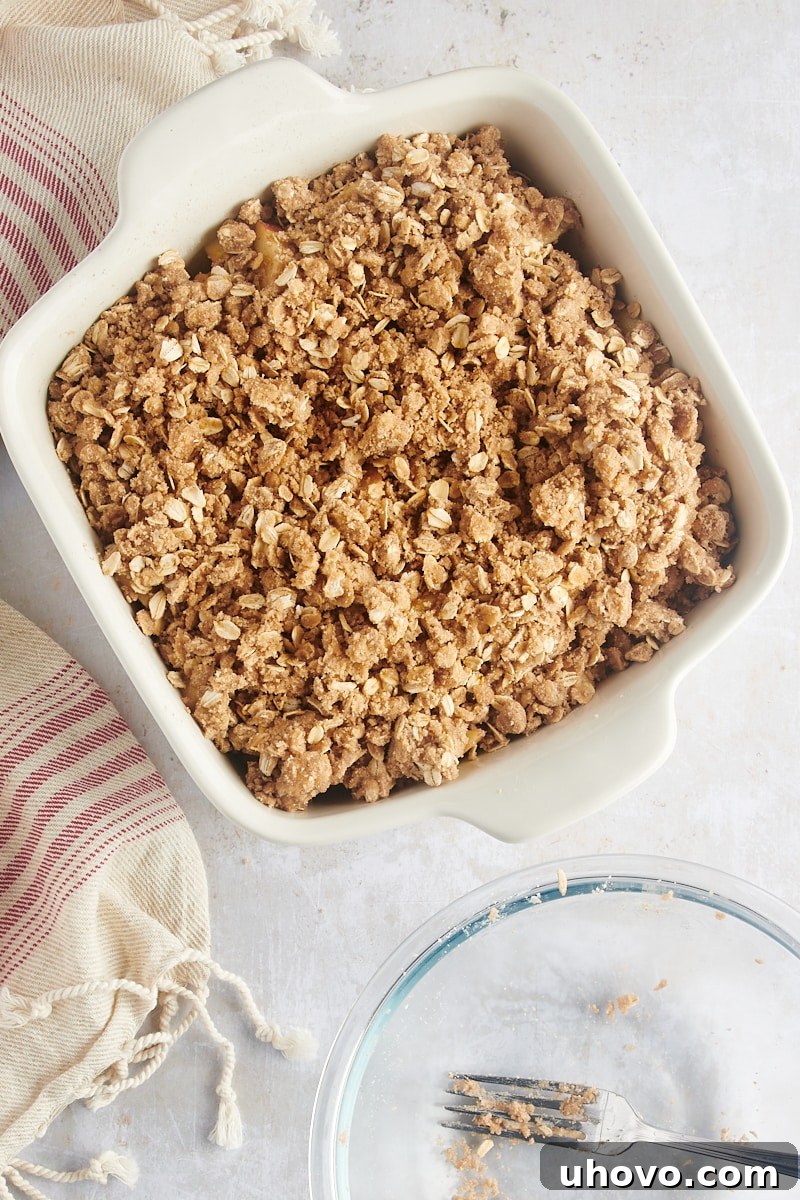 A baking dish with sliced apples completely covered by an even layer of spiced oat streusel topping, ready for baking.