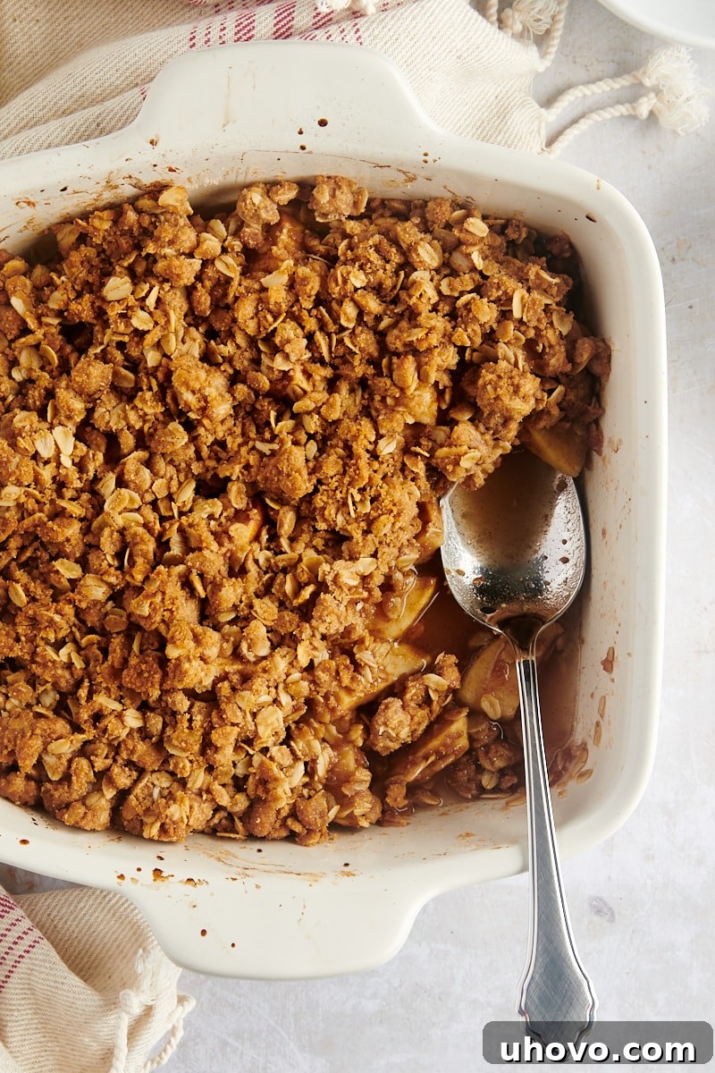 A portion of apple crisp scooped out of the pan, with a serving spoon still in the empty space, ready to be enjoyed.