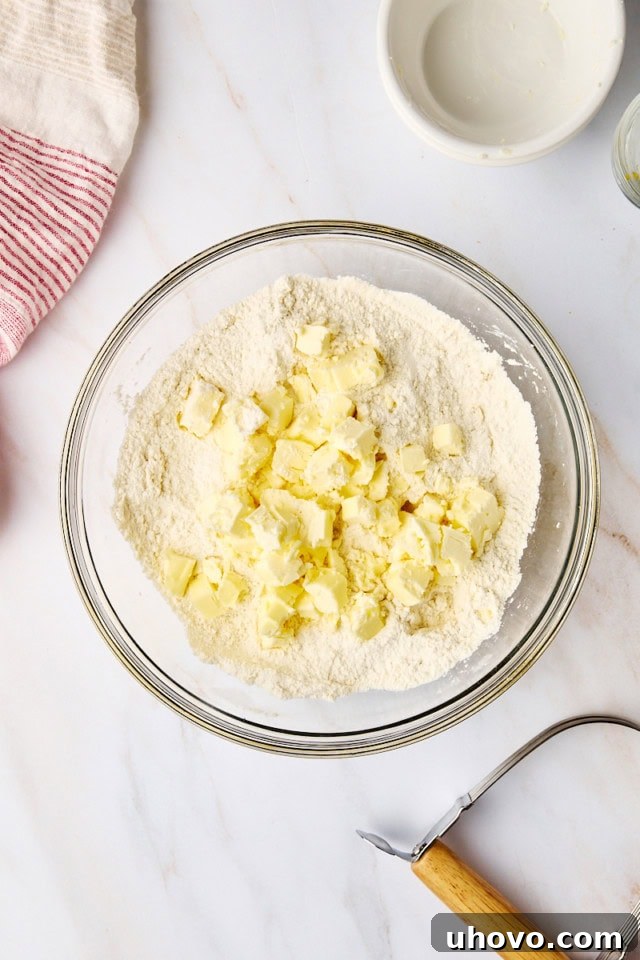 A close-up, overhead view showing cold, cubed butter being added to the dry ingredients, ready to be cut in for the biscuit dough, highlighting the crucial step for flakiness.