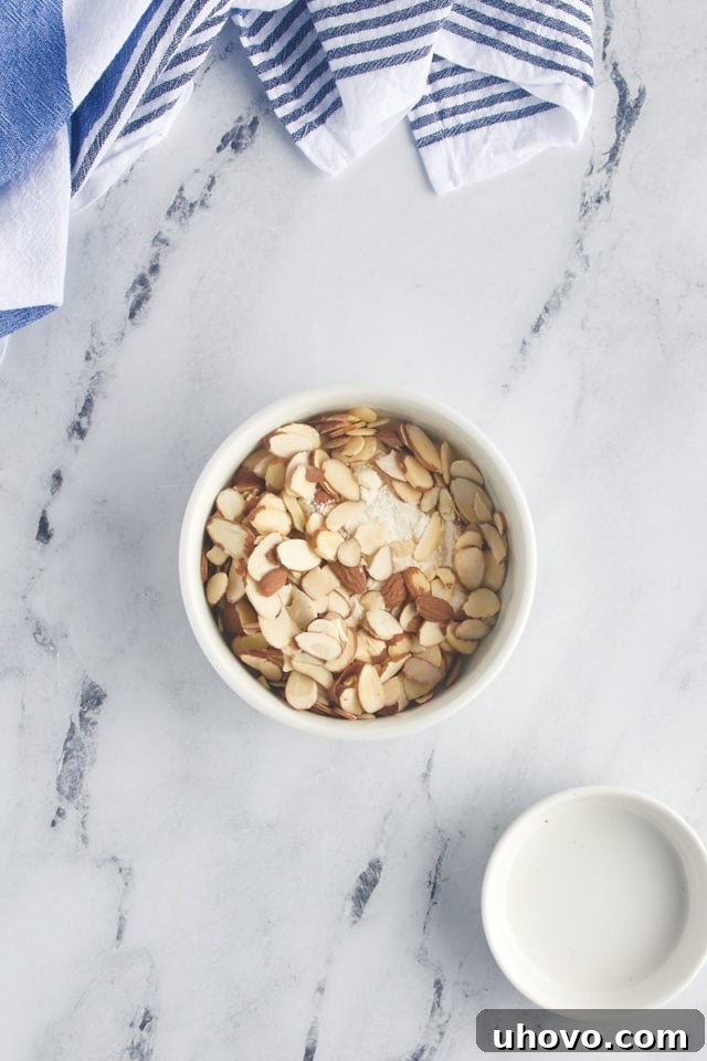 Sliced almonds being folded into the reserved crumb mixture in a small bowl, creating the delicious almond streusel topping.
