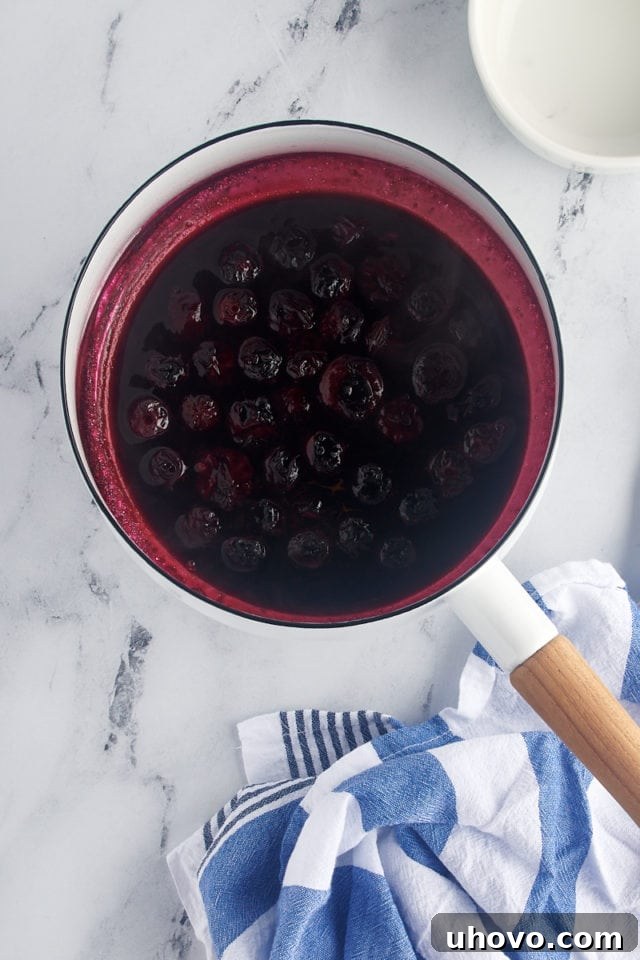 Overhead view of the blueberry topping thickening in a saucepan after cornstarch slurry has been added, showing a rich, glossy, and jam-like consistency.