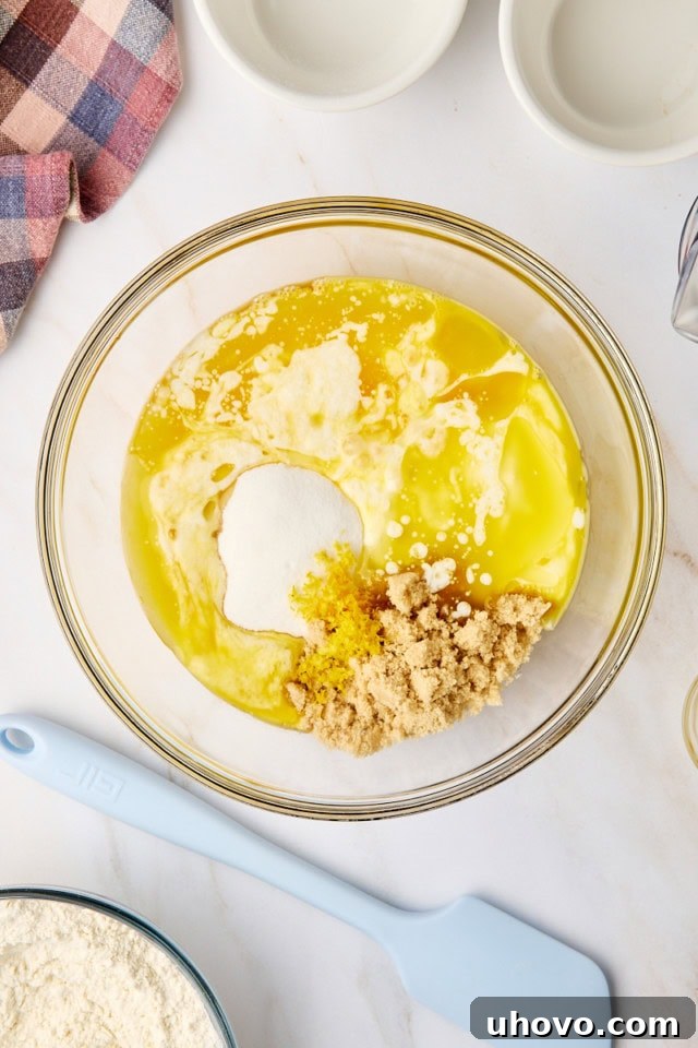 An overhead view of wet ingredients for blackberry muffins, including eggs, buttermilk, sugars, and melted butter, mixed together in a clear glass mixing bowl.