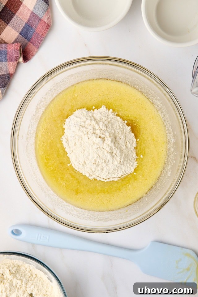 An overhead view of the dry ingredients being added to the wet ingredients in a glass mixing bowl, creating the initial muffin batter.