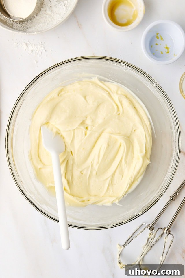 Overhead view of a beautifully whipped, creamy lemon cream cheese frosting in a clear glass mixing bowl, ready for piping.
