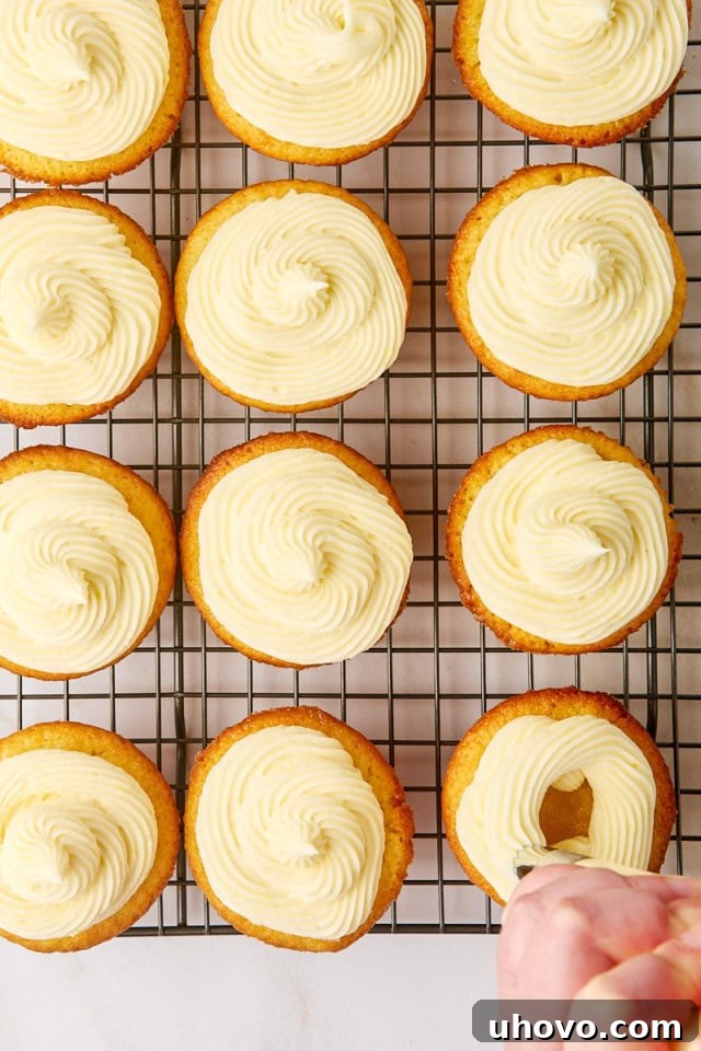 Overhead view of fluffy lemon cream cheese frosting being expertly piped onto a cooled lemon cupcake, creating a beautiful swirl.