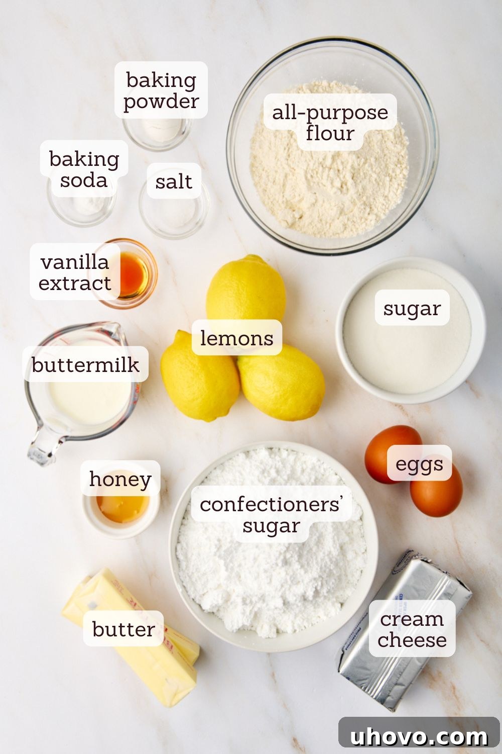 Overhead shot of fresh ingredients laid out on a white surface, including lemons, flour, sugar, butter, and eggs, ready for baking lemon cupcakes.