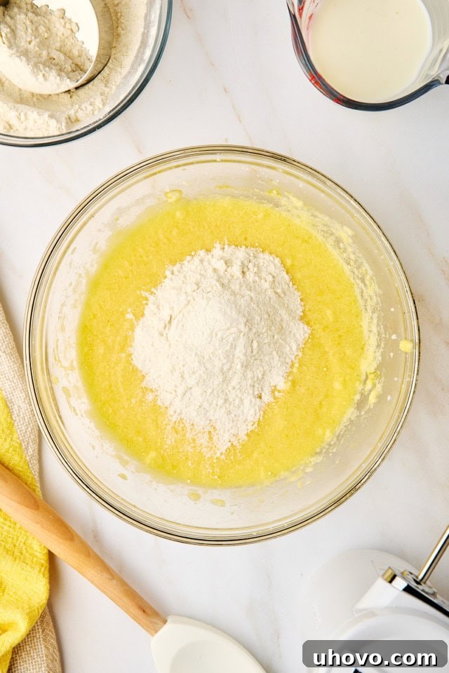 Overhead view showing dry flour mixture being added to the wet ingredients in a mixing bowl for lemon cupcakes, illustrating the alternating method.