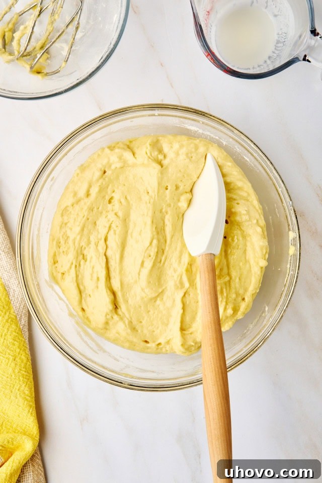 Overhead view of a smooth, pale yellow lemon cupcake batter in a clear glass mixing bowl, perfectly mixed and ready for baking.
