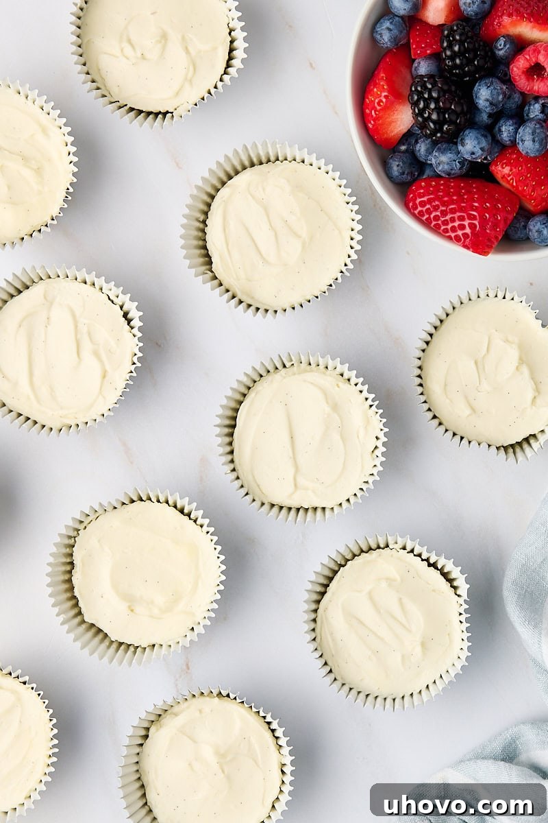 An inviting overhead view of finished mini no-bake cheesecakes artfully arranged alongside a bowl of fresh, vibrant berries on a clean marble countertop, ready for serving.
