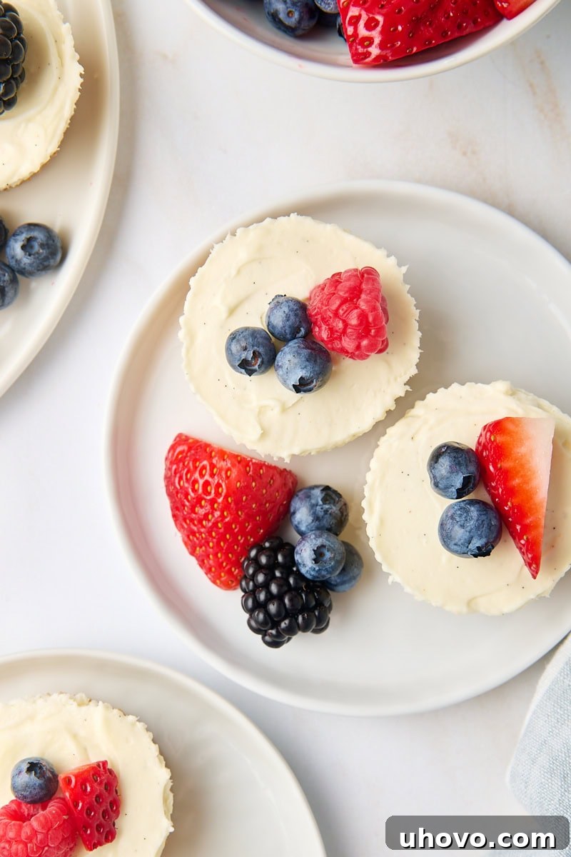 An overhead shot showcasing multiple mini no-bake cheesecakes, each artfully topped with an assortment of fresh berries, arranged beautifully on white plates for an elegant presentation.