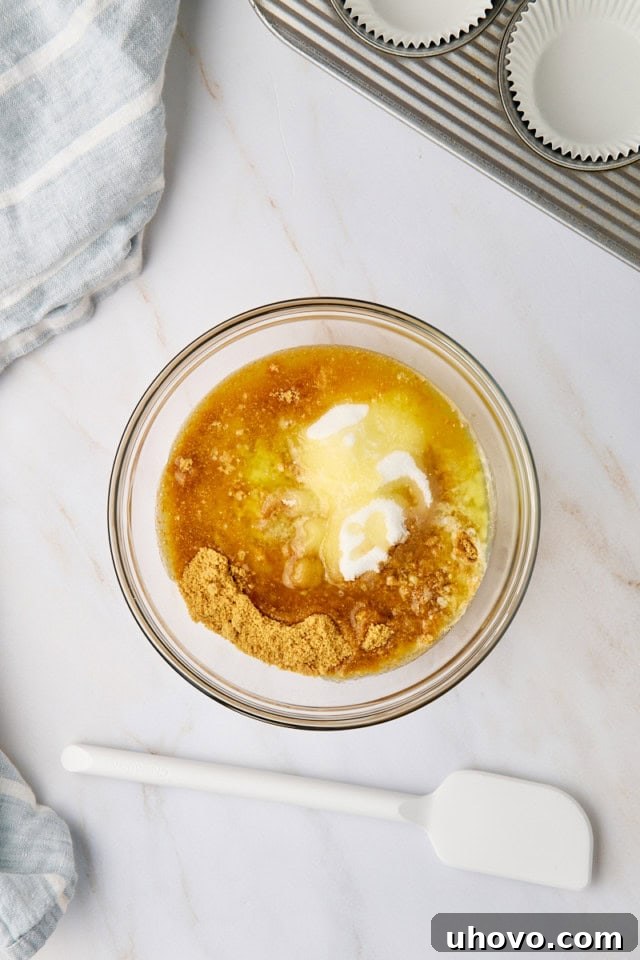 An overhead view of graham cracker crumbs, granulated sugar, and melted butter perfectly combined in a clear glass mixing bowl, ready for the crust preparation.