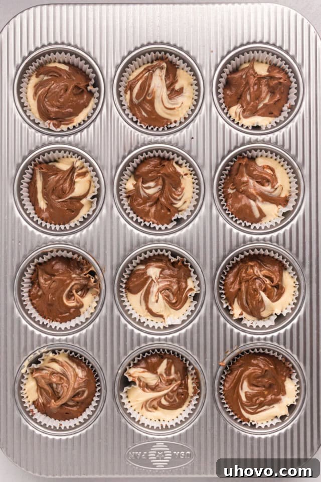 An overhead view of marble cupcakes neatly arranged in a muffin pan, showcasing the subtle swirls of batter before baking, ready to be placed into the oven.