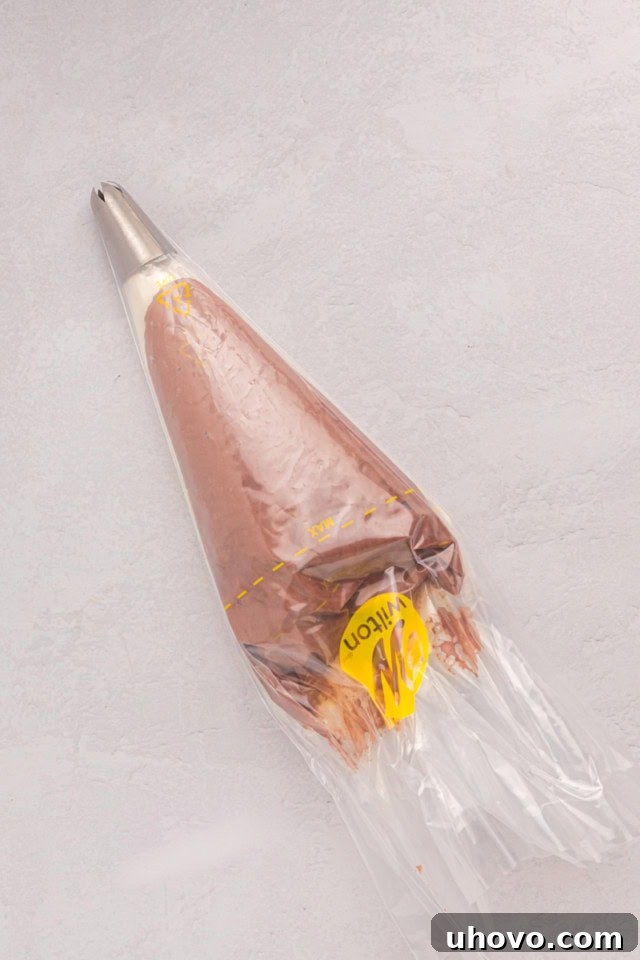 An overhead view of two small piping bags, one filled with vanilla buttercream and the other with chocolate buttercream, being placed side-by-side into a larger piping bag, ready for two-tone frosting.