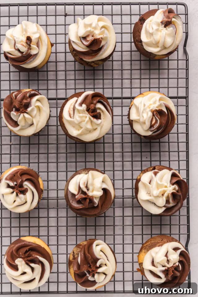 An overhead view of freshly frosted marble cupcakes cooling on a wire rack, each adorned with a beautiful two-tone swirl of chocolate and vanilla buttercream, showcasing the final presentation.