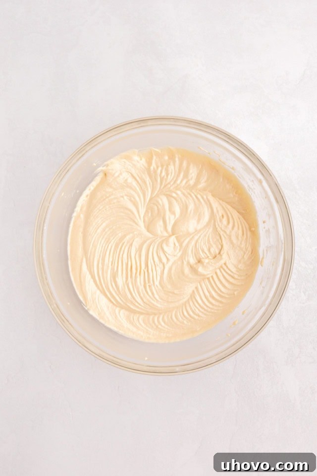 An overhead view of a smooth, light vanilla cupcake batter resting in a large glass mixing bowl, perfectly mixed and ready for the next step of division.
