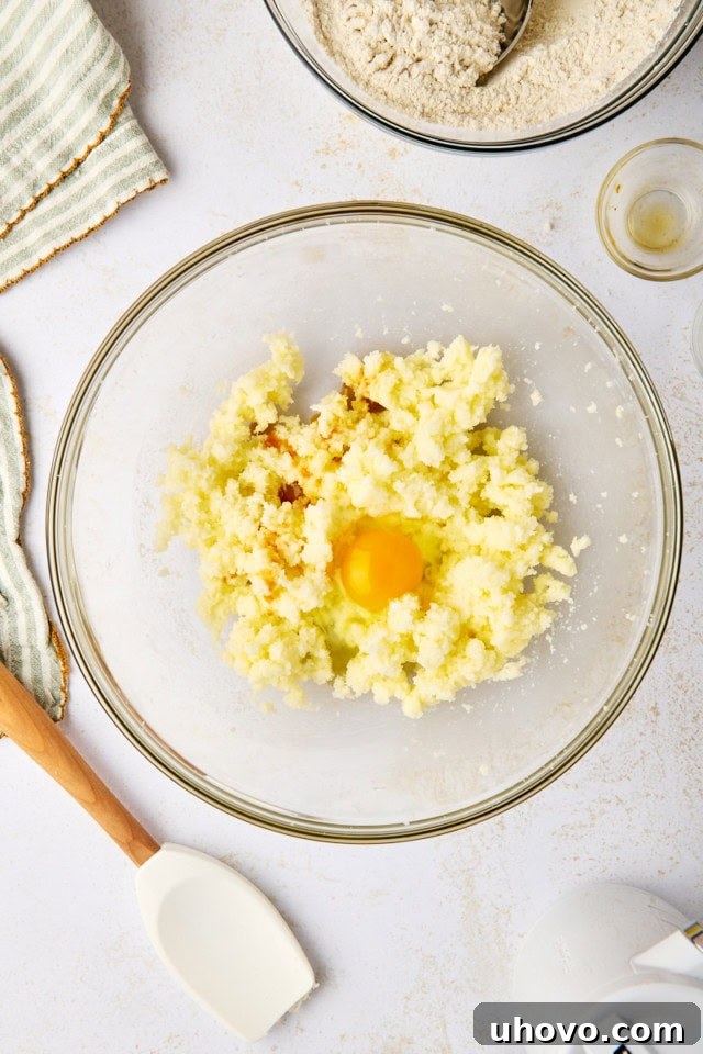 overhead view of egg , almond extract, and vanilla extract added to creamed butter and sugar in a glass mixing bowl