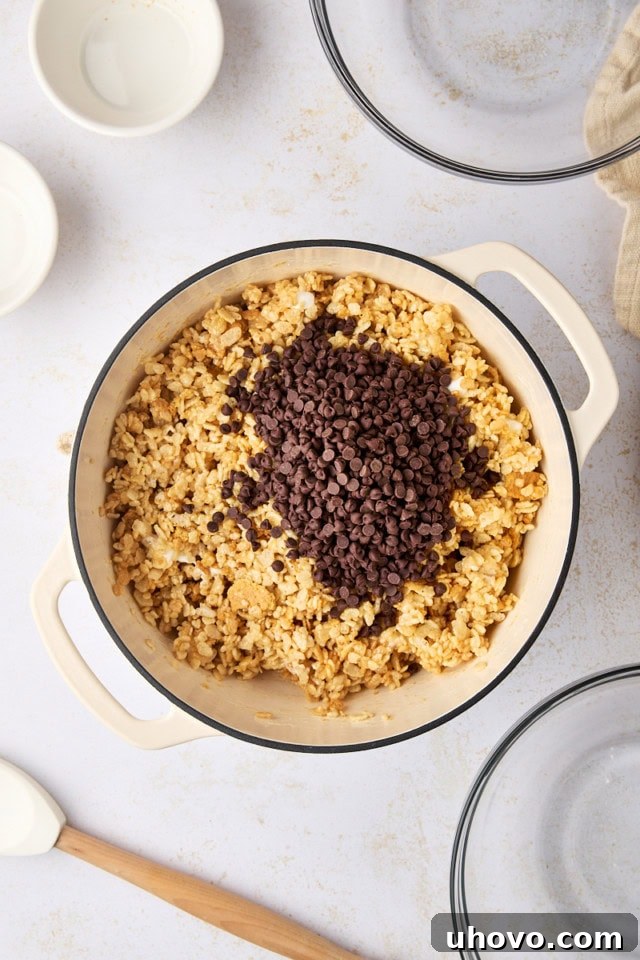 overhead view of chocolate chips added to s'mores rice crispy treat mixture in a saucepan