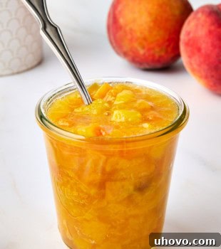 peach compote in a glass jar with a spoon resting inside