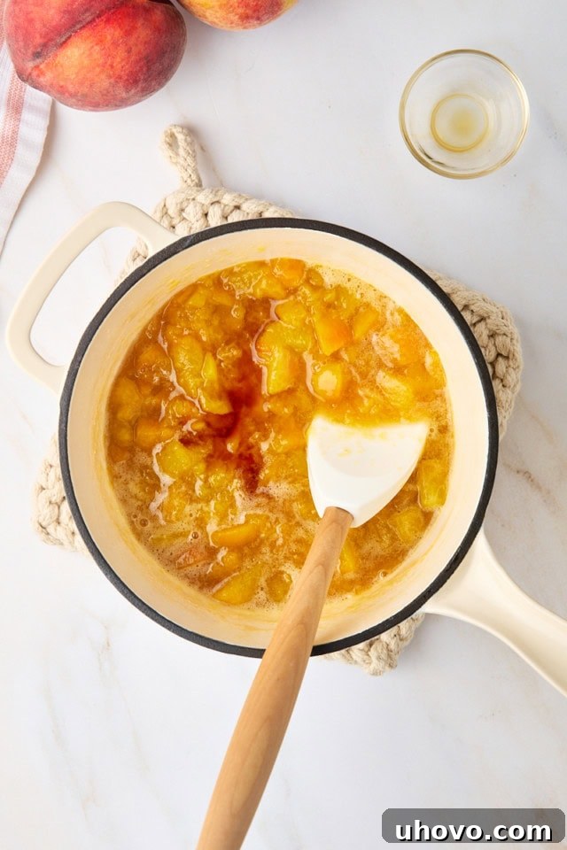 Overhead view of vanilla extract being stirred into the warm peach compote in a saucepan, after it has been removed from heat.