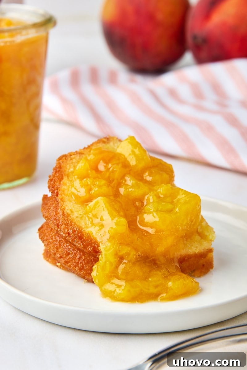 A generous serving of peach compote drizzled over a slice of light pound cake, presented on a white plate, ready to be enjoyed.