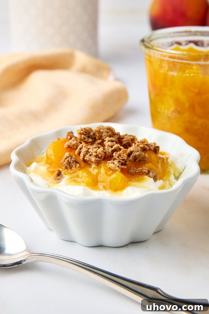A white bowl filled with creamy yogurt topped with generous spoonfuls of peach compote and crunchy granola, creating a wholesome and delicious breakfast.