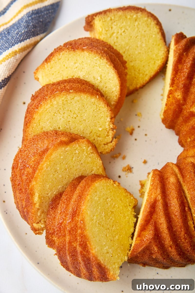 A partially sliced golden cornmeal pound cake resting on an elegant white cake plate, ready to be enjoyed.