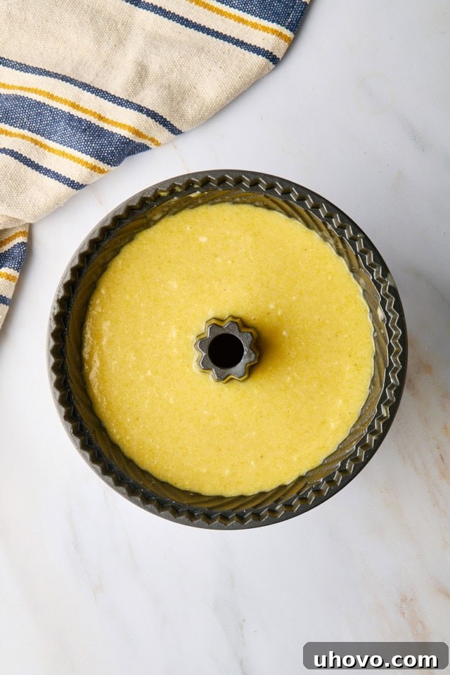An overhead view of the smooth cornmeal pound cake batter being carefully transferred and spread evenly into a prepared Bundt pan, ready for baking.