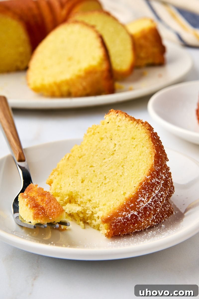 A close-up of a slice of cornmeal pound cake on a white plate, with a fork taking a bite, showing the tender crumb and rustic texture.