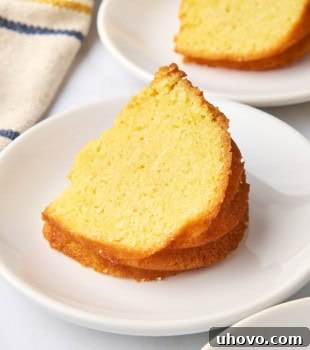 A delectable slice of cornmeal pound cake presented on a white plate, with another tempting slice blurred in the background, showcasing its golden hue.