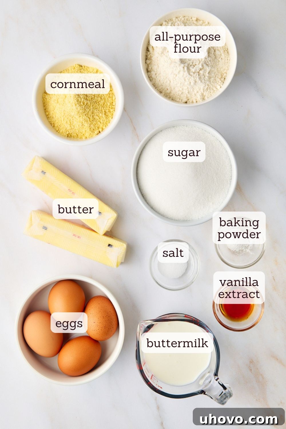 An overhead shot showcasing the key ingredients neatly arranged for making cornmeal pound cake: flour, cornmeal, butter, eggs, sugar, and buttermilk.