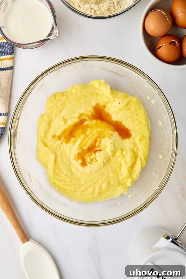 An overhead view of fragrant vanilla extract being poured into the smooth, yellow cake batter, ready to infuse its warm aroma.