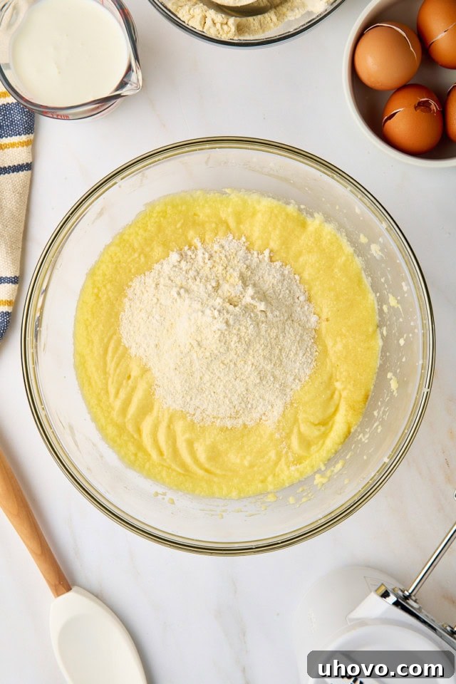 An overhead view of the dry ingredients being gradually added to the wet mixture for the cornmeal pound cake, ensuring careful incorporation.
