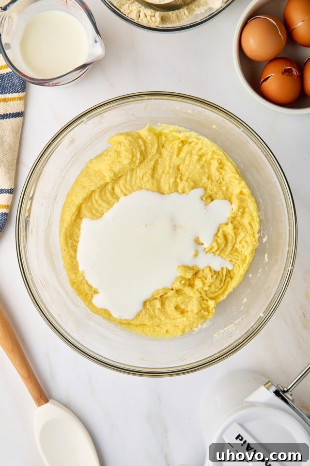 An overhead view of rich buttermilk being carefully poured into the pound cake batter, alternating with dry ingredients for a moist and tender result.