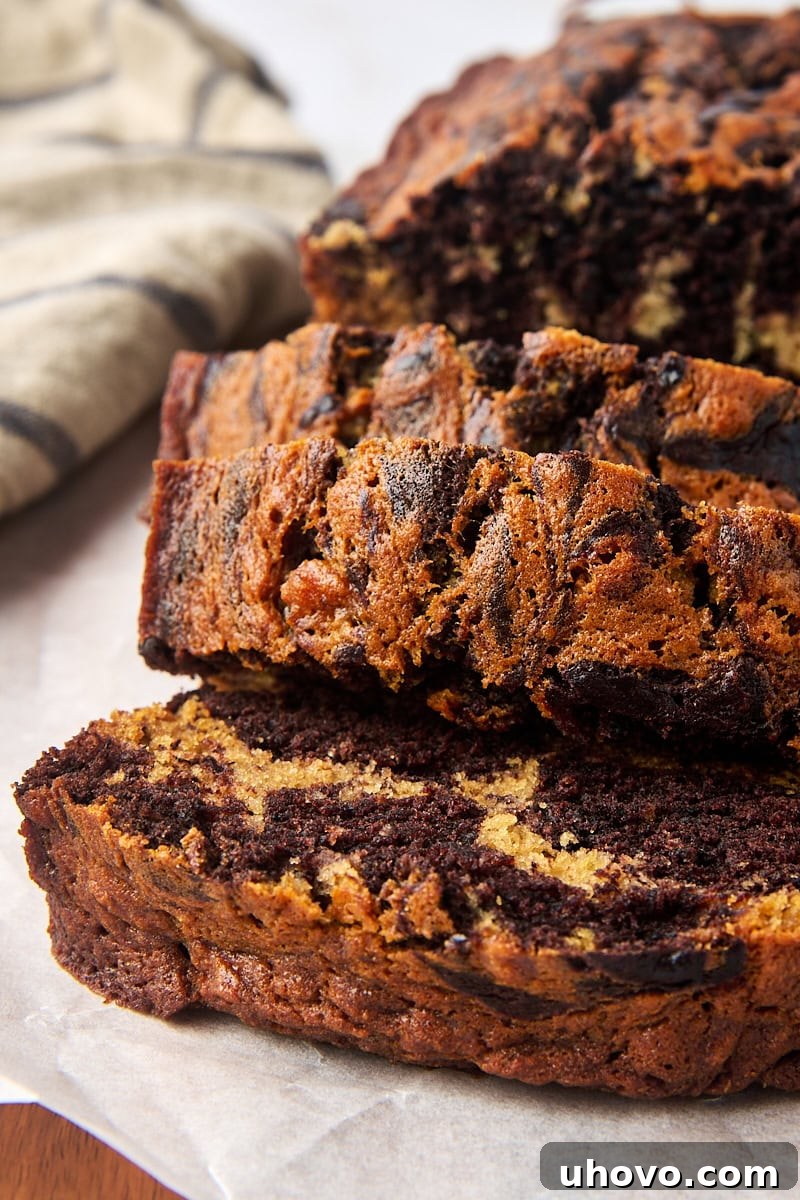 Slices of moist marbled chocolate banana bread on parchment paper, showcasing the beautiful chocolate and banana swirl.
