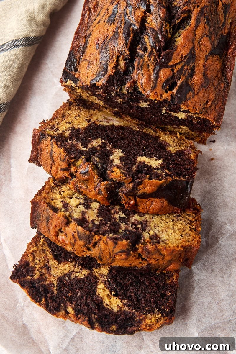 Overhead view of a partially sliced loaf of marbled chocolate banana bread, showing the intricate chocolate and banana swirls, presented on parchment paper.