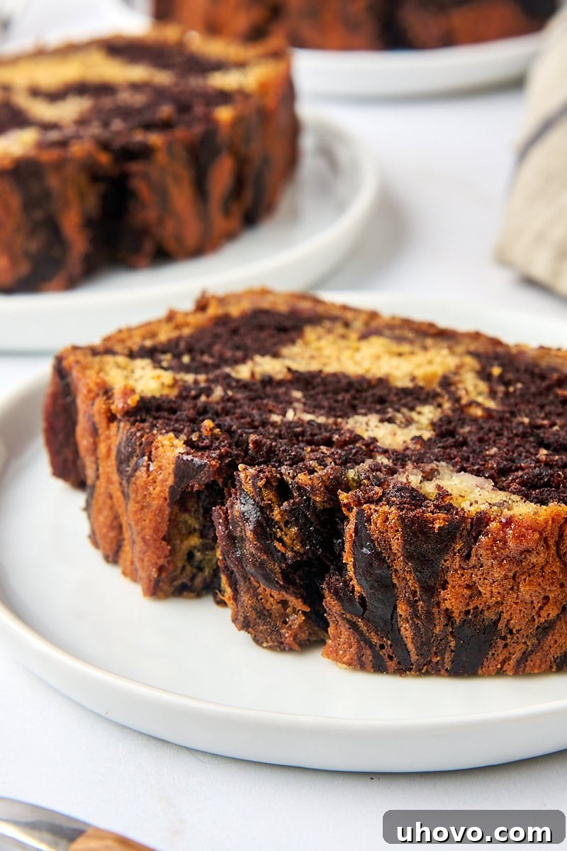A beautiful slice of marbled chocolate banana bread displayed on a white plate, with other slices in the soft background, highlighting its rich color and inviting texture.