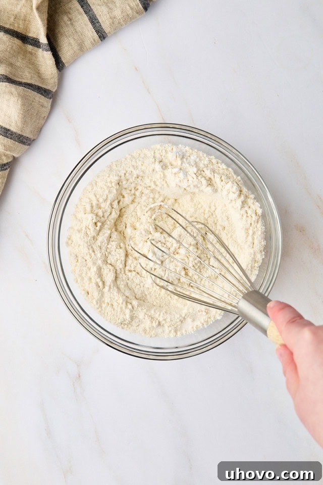 Overhead view of all-purpose flour, baking soda, and salt being whisked together in a clear glass mixing bowl, forming the dry ingredients mixture.
