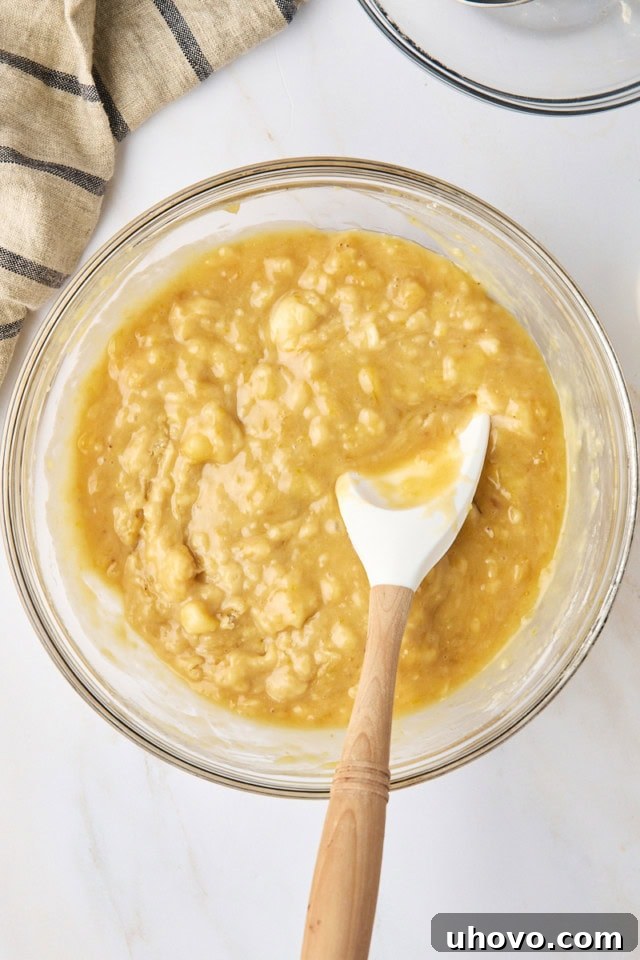 Overhead view of the light brown banana bread batter in a clear glass mixing bowl after the dry and wet ingredients have been combined, showing a slightly lumpy texture.