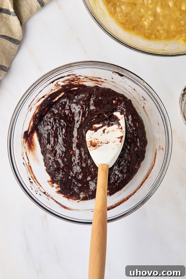 Overhead view of the dark chocolate banana bread batter in a glass mixing bowl, with a small amount of milk added to thin it to the correct consistency for swirling.
