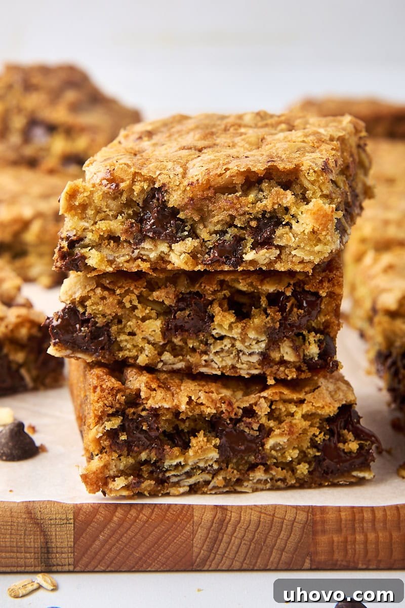 Stack of three homemade oatmeal cookie bars with melty chocolate chips, resting on a parchment-covered cutting board.