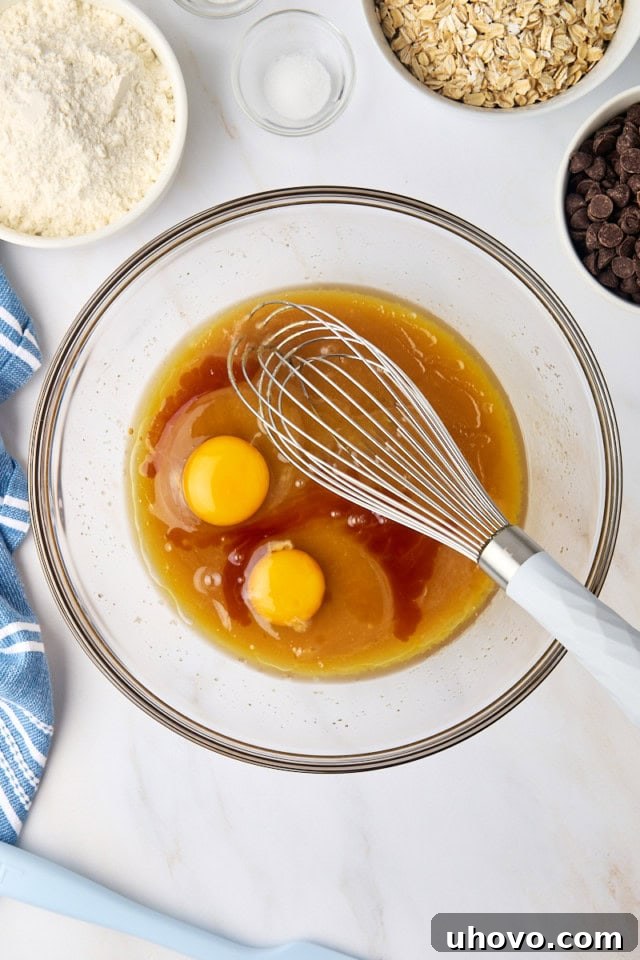 Two large eggs and a pour of vanilla extract being added to the butter and sugar mixture in a glass bowl.