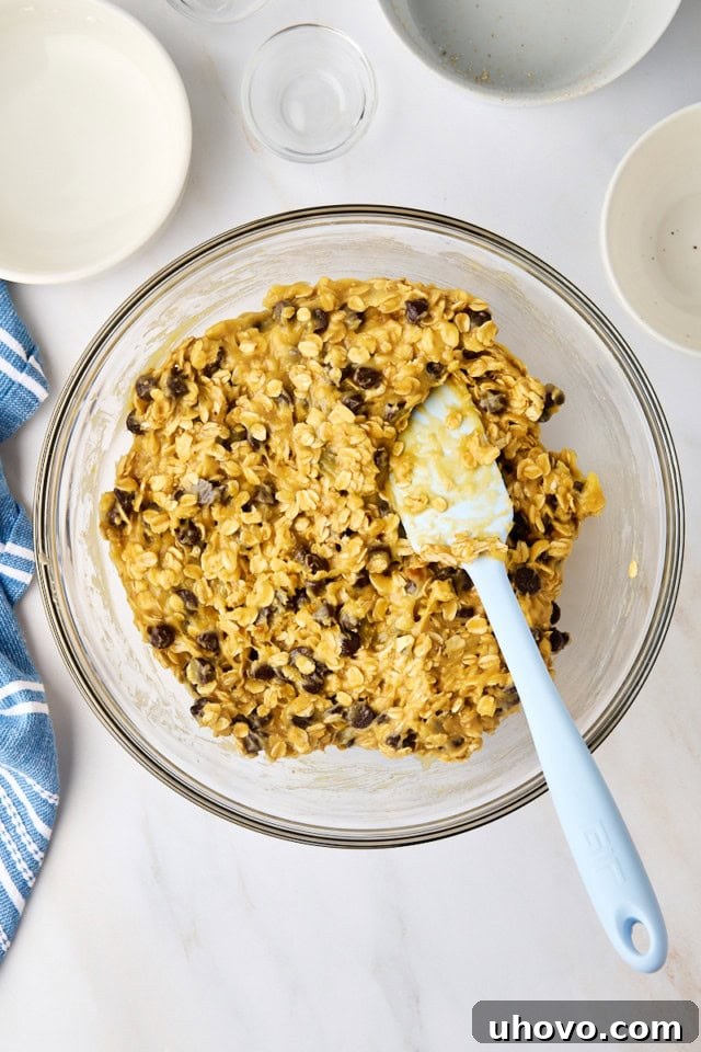 Close-up overhead view of the completed oatmeal cookie bar batter in a glass mixing bowl, showcasing the oats and chocolate chips.